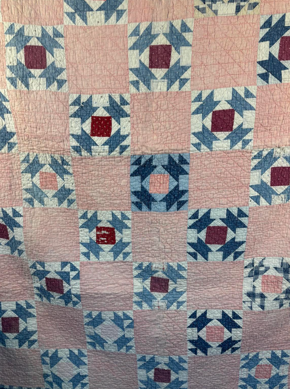 Quilt with geometric pattern featuring squares and diamonds in blue, red, and beige.